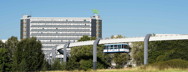 Das Mathegebäude mit TU-Logo und die H-Bahn