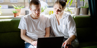 Zwei Studierende arbeiten am Laptop, auf einem Sofa sitzend.