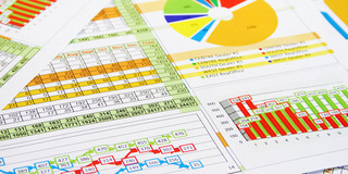 Papierseiten mit Tabellen, Kreis-, Säulen- sowie Graphdiagrammen liegen übereinander.